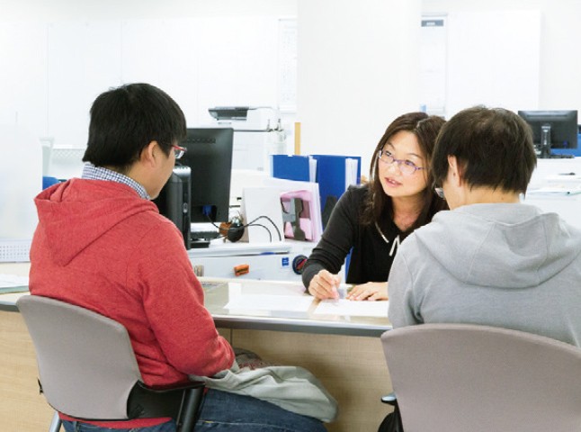 写真：女性の大学職員と資料を見ながら話している2人の男子学生